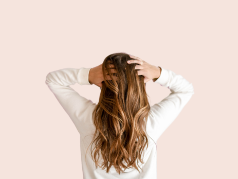 Woman touching her hair wearing a white sweater facing away from the camera on a pink background